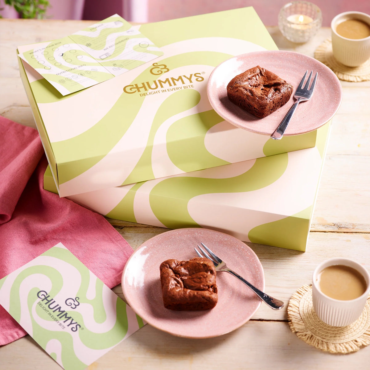 A Chummys brownie box with a square on a plate and a cup of tea